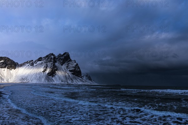 White foamy waves on the beach of Stokkness, behind snowy rocky slopes of Vestrahorn, near Höfn,