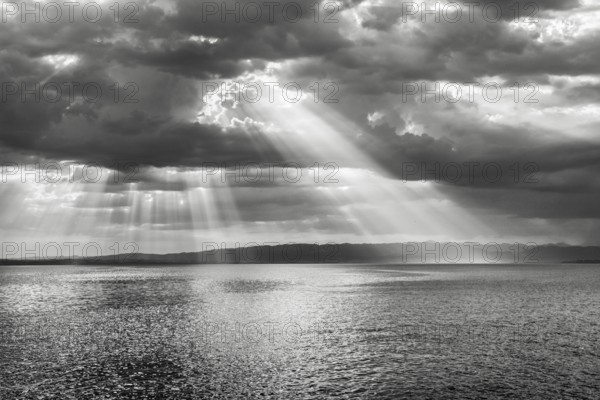 Tyndall effect over Lake Constance, sun rays break through cloudy sky and reflect on the water,