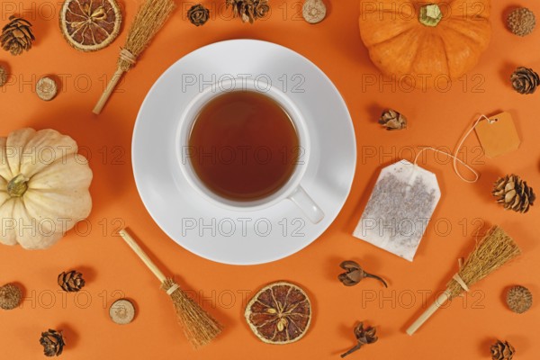 Cup of tea surrounded by seasonal fall decoration like pumpkins and orange slices on orange