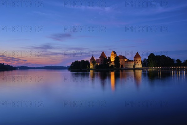 Trakai Island Castle in lake Galve illuminated in twilight reflecting in peaceful water, Lithuania,