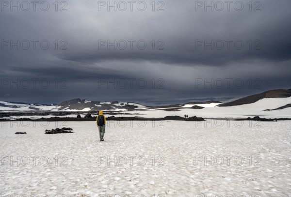 Hikers in snow-covered volcanic landscape with volcanic sand and petrified lava, crater of Askja
