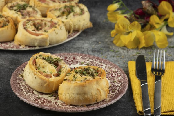 Baked dough snails with sausage and cheese on plates with cutlery and floral decorations in the