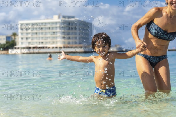 Mother and son holding hands and splashing in the clear turquoise water of estanys beach in