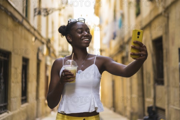 Smiling young african american woman talking selfie showing a delicious milkshake in the city