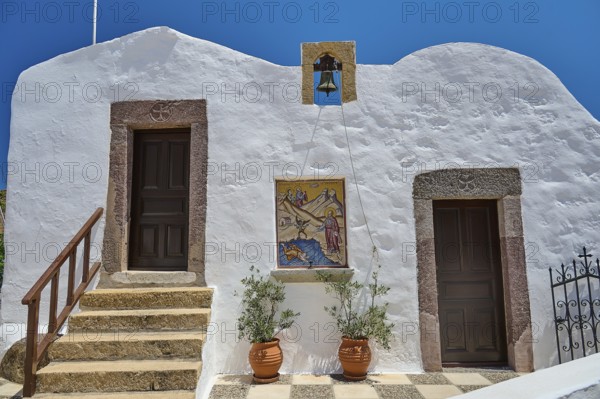 Traditional Greek building with white wall, two doors, bell and staircase under blue sky,