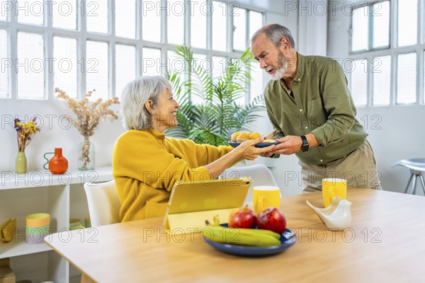 Senior man serving breakfast to share with his wife while she is using digital tablet sitting on