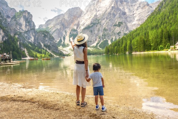 Mother pointing at the landscape while holding her son's hand on the shore of lake braies in the