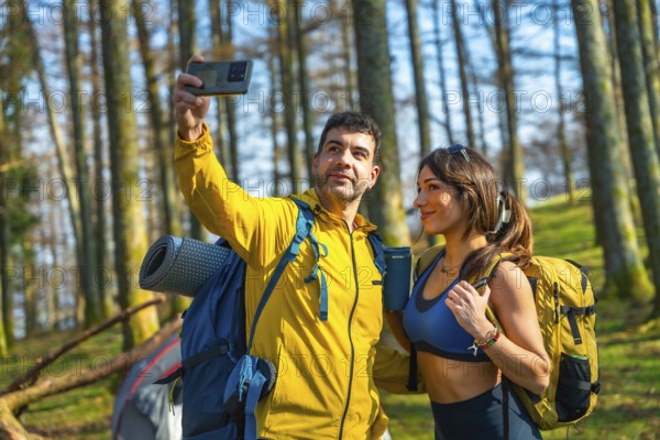 Couple taking a selfie with smartphone in the woods during camping trip, wearing backpacks and