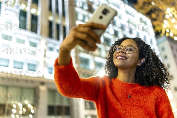 Smiling woman capturing a selfie with her mobile phone in a vibrant urban city, surrounded by