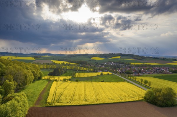 View of Tiftlingerode between blooming rape fields in rain and sunshine, Duderstadt, Lower Saxony,