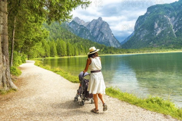 Tourist walking with her baby along the scenic shores of lake dobbiaco, surrounded by the stunning