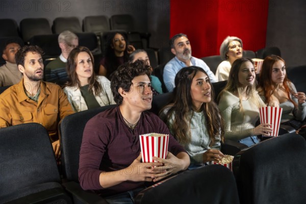 People of different ages and ethnicities are watching a film in a movie theater, holding popcorn