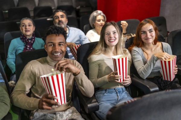 Multi ethnic group of friends enjoying a film at the movie theater, sharing laughter and munching