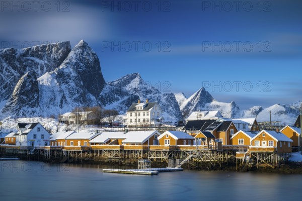Traditional yellow rorbuer huts on the island of Sakrisøy, snow-capped mountains in the background,