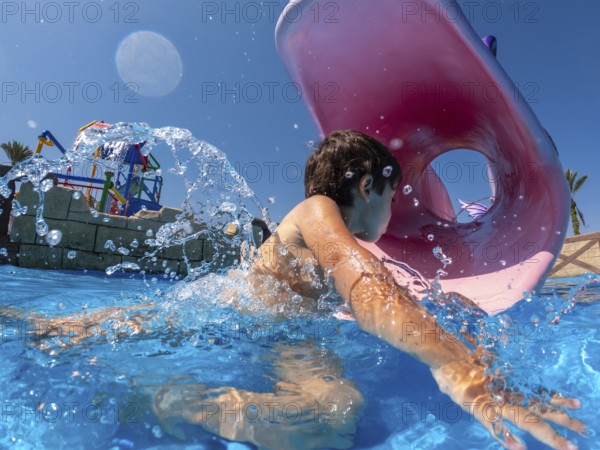 Child having fun swimming through inflatable ring in water park during summer vacation, enjoying