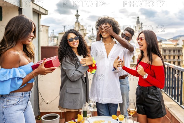 Multiracial group of friends covering eyes of a man giving her a present in a rooftop party