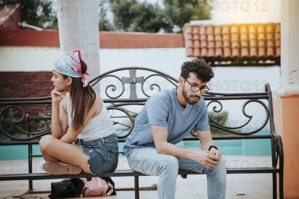 Unhappy couple sitting back to back on bench. Concept of couple problems and crisis. Upset young