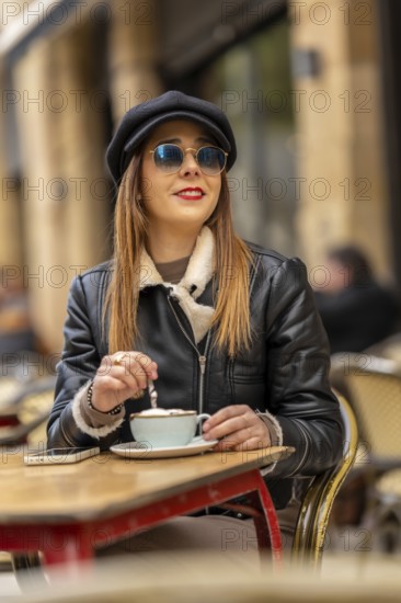 Fashionable woman wearing sunglasses and a hat savoring a cappuccino at a parisian cafe, enjoying