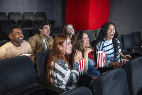 Group of young people enjoying a movie at the cinema, sharing laughter and smiles while munching on