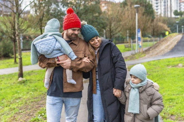 Smiling parents walking with their children in a park on a chilly winter day, enjoying moments of