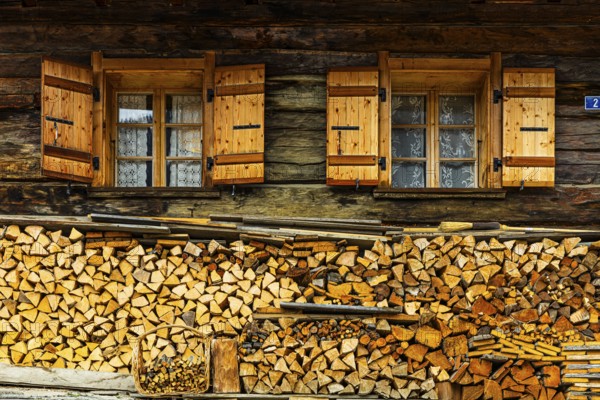 Old windows with shutters on an old farmhouse, firewood piled up in front, mountain village of