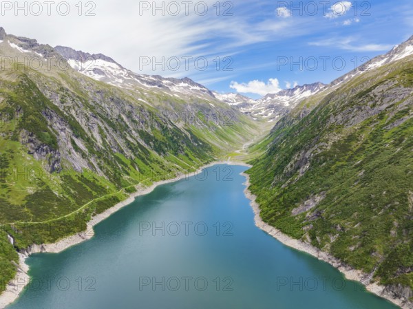 Mountain landscape with a blue lake in the centre, surrounded by lush greenery and snow-capped