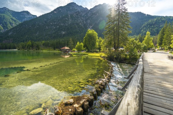 Sunlight illuminating the crystal clear waters of lake dobbiaco, with a wooden bridge and the