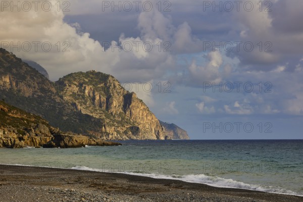 Rocky cliffs on the coast with foamy waves and a dramatic cloudy sky in the distance, south coast,