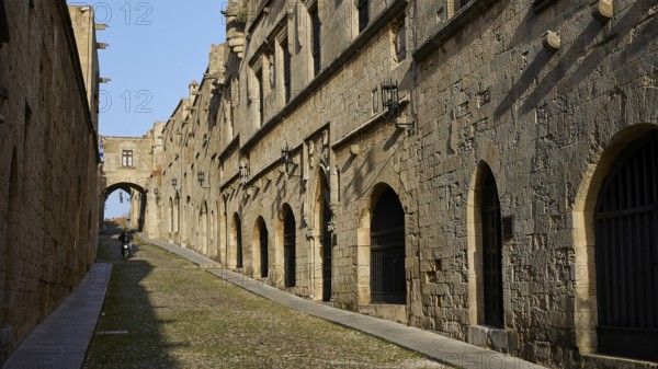 An ancient street lined with historic buildings with arcades in sunny weather and blue skies, moped