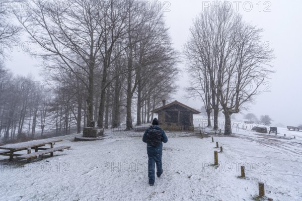 A young man walking next to the refuge of mount aizkorri in gipuzkoa. Snowy landscape by winter