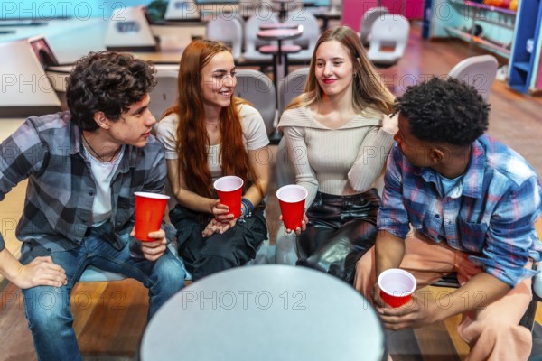 Four young friends enjoying a casual hangout at the bowling alley, holding red cups and engaging in