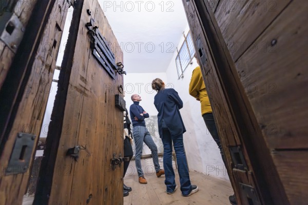 Several people standing in a room with large wooden doors and a historical appearance, Prison