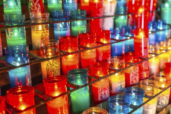 Colorful votive candles burning on a metal rack inside the montserrat monastery, creating a warm