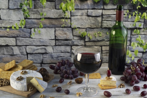 Wine glass and bottle of red wine surrounded by cheese, grapes, nuts and crackers in front of a