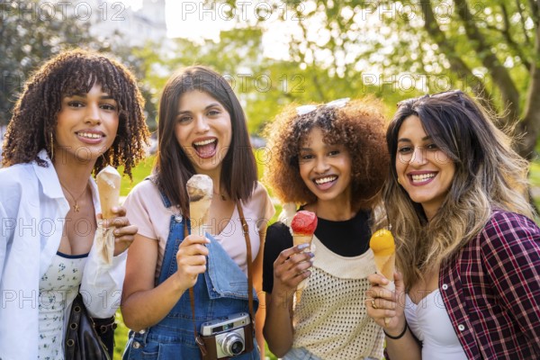 Four cheerful young women enjoying ice cream cones together in a park, celebrating summer and