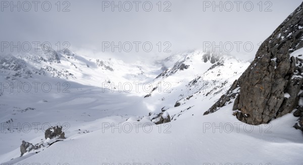 View of cloudy valley from the summit of Piz Laviner, mountain landscape in winter, Grisons Haute