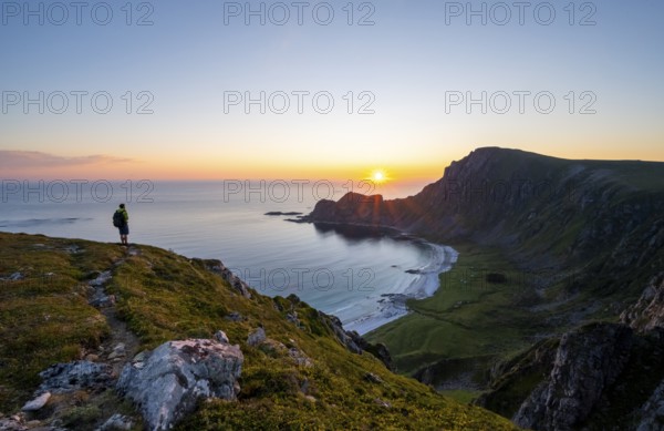 Mountaineer in front of view of coastal landscape at sunset, cliffs and summit of Måtind or