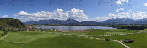 Expansive landscape with a view of Lake Hopfensee and mountains, surrounded by green meadows and a