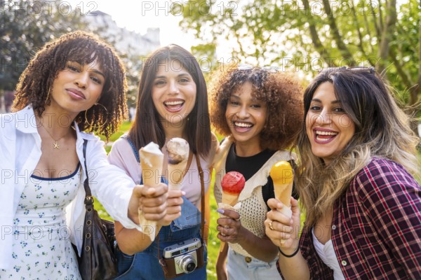 Four cheerful young women enjoying ice cream cones together in a park, celebrating friendship and