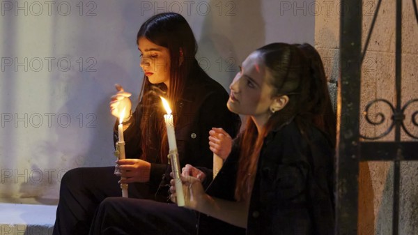 Two girls sit by candlelight, their faces marked by calm and serenity as they quietly contemplate