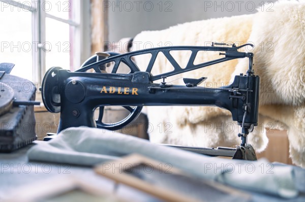 An antique Adler sewing machine in a studio with sewing accessories and leather material, Calw