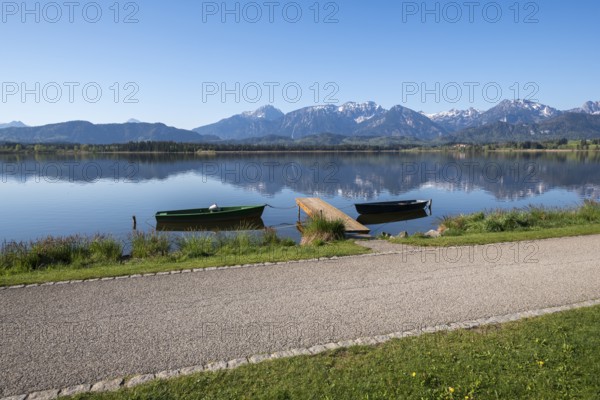 Calm lake with green and black boats, jetty and alpine landscape in the background, Hopfen am See,
