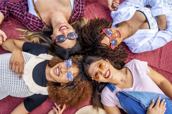 Four diverse young women lying together on a vibrant red blanket, smiling brightly at the camera