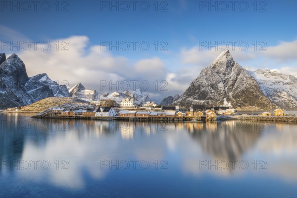 Traditional yellow rorbuer huts on the island of Sakrisøy, snow-capped mountains in the background,