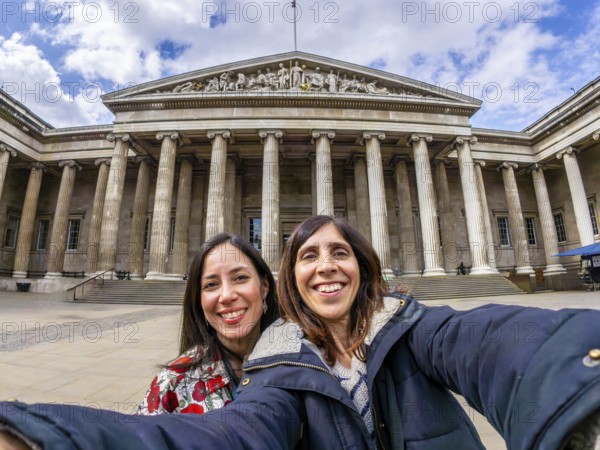 Two happy female tourists are taking a selfie with a fisheye lens in front of the british museum in