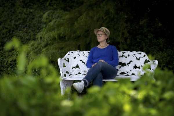 Elderly woman, wearing a sun hat, sitting on a white park bench, pensive, Mainau Island, Constance