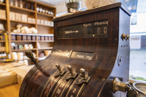 Antique cash register in a shop with ceramics and wooden shelves in the background, Calw Tannery