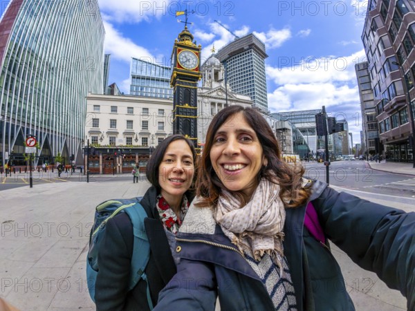 Two happy tourists taking a selfie with a fisheye lens in front of a historic clock tower in