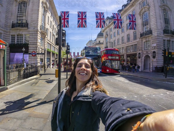 Young woman taking a selfie in london with union jack flags and a red double decker bus in the