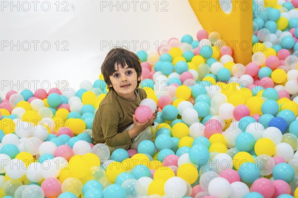 Young boy enjoying playtime in a vibrant ball pit, surrounded by colorful plastic balls in a lively